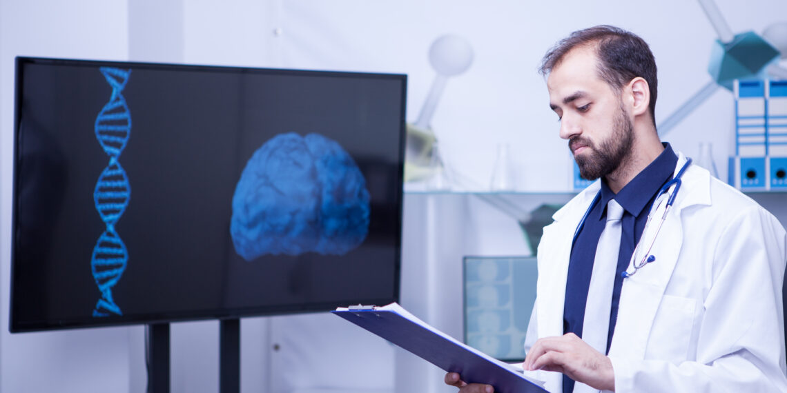 Confident young doctor with a clipboard in his hands standing by a monitor with a brain graph