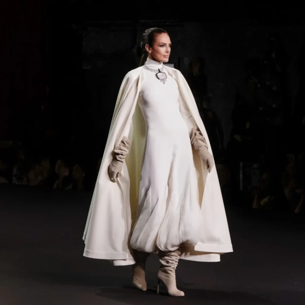 White couture cape look with statement jewel necklace and taupe slouch