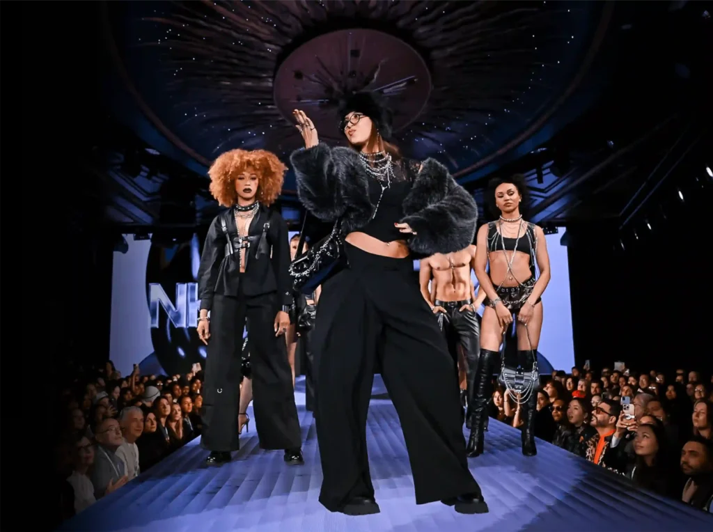 performer walking in black fur and wide-leg trousers, full crowd on both sides