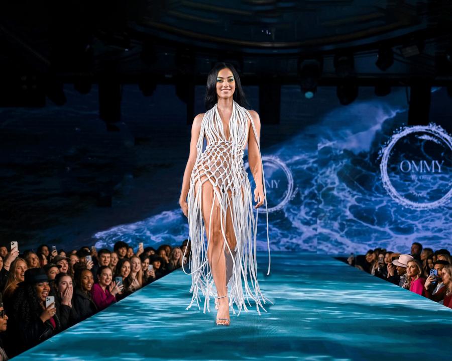 white knotted macramé dress on an ocean-projected runway, OMMY branding visible