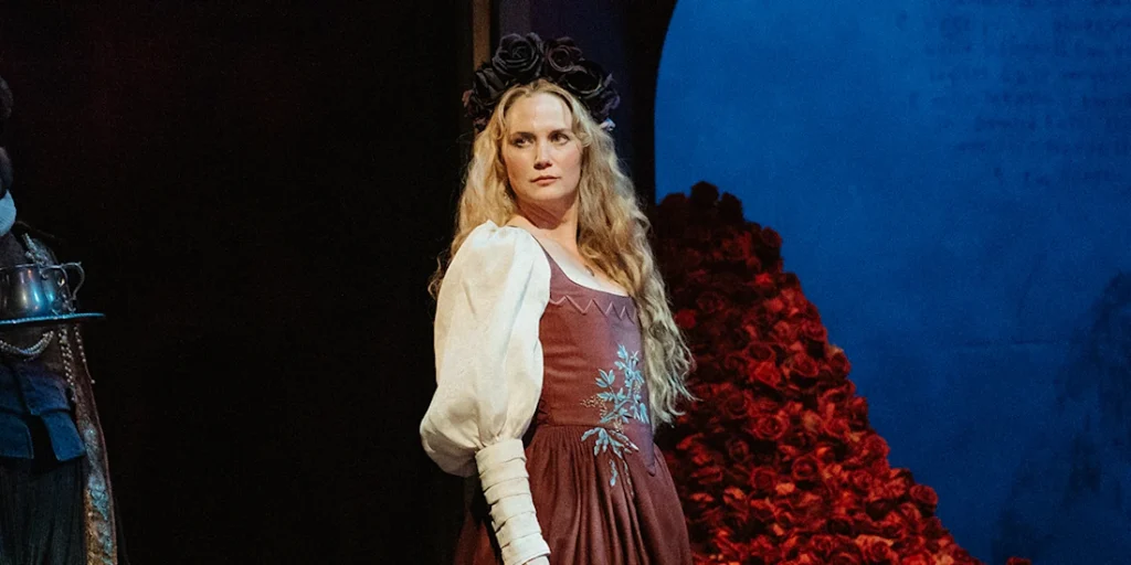 Nettles crowned in black roses before a cascade of red ones, the production's design language in one frame