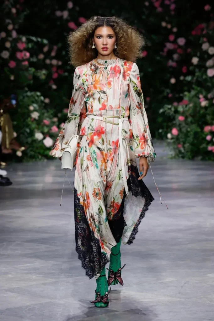 Model in a belted long-sleeve dress in the Luisa floral print with a black lace hem, green tights, and butterfly-embellished shoes