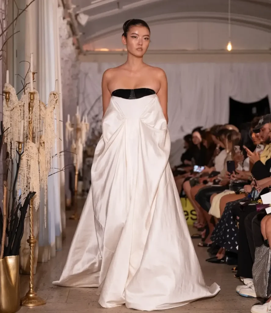 Model in a strapless ivory satin gown with a black velvet band at the bust and voluminous draped hips