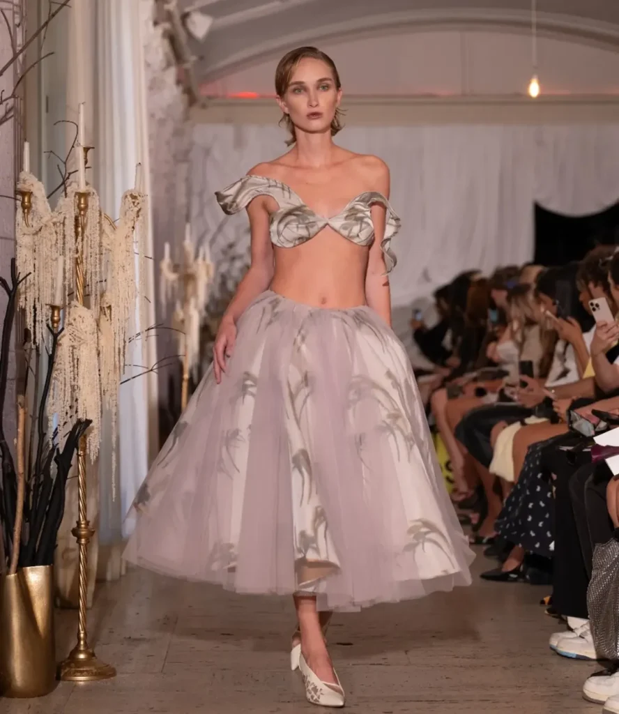 Model in an off-the-shoulder printed satin cup top with a lavender tulle tea-length skirt marked with grey brushstrokes