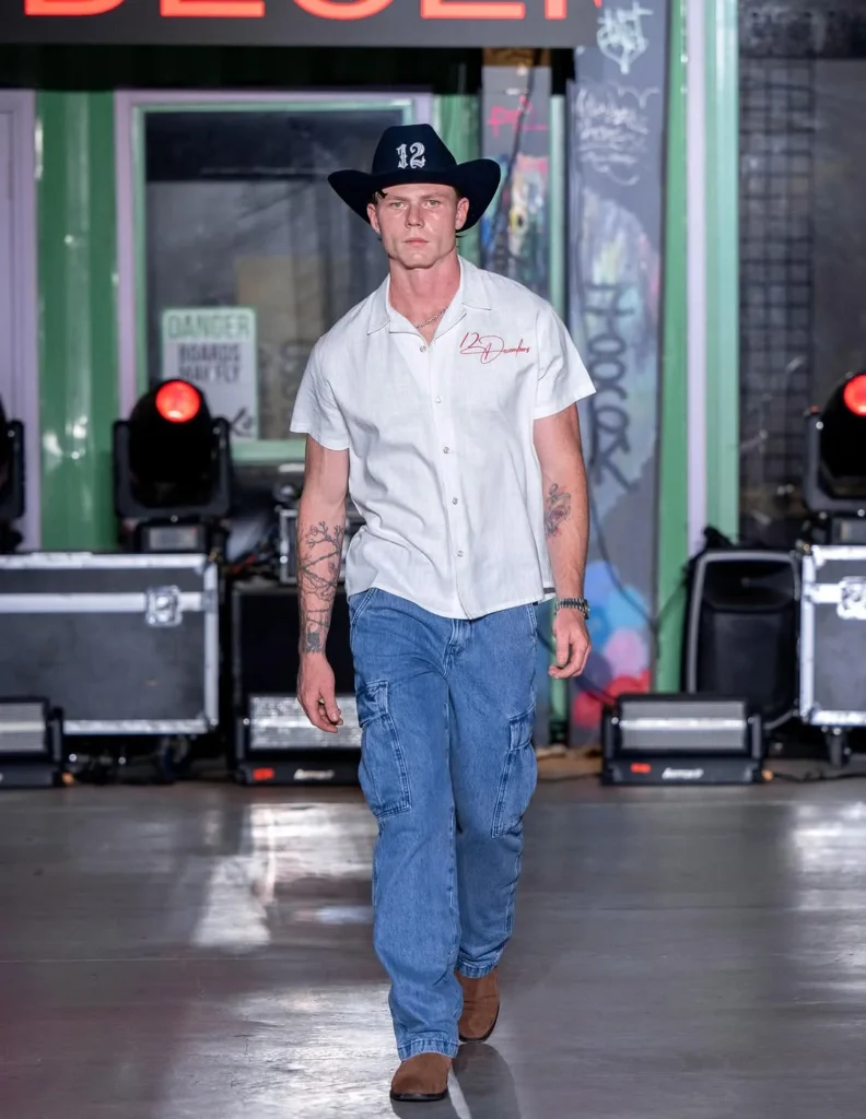 black felt cowboy hat embroidered with a white camp shirt and blue cargo jeans